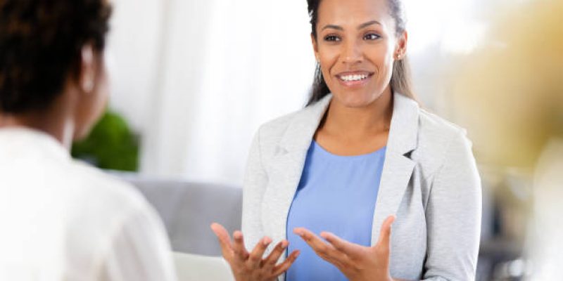 During a counseling session, an unrecognizable patient listens carefully as the female therapist speaks and gestures to communicate an idea.